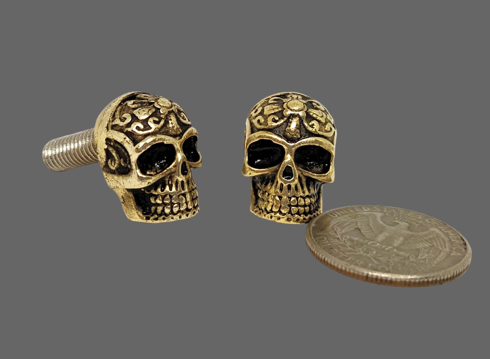  Two gold skull-shaped screw caps with black eyes and detailed carvings. 